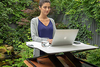 Image of a woman using her laptop with the Oploft-Sit-Stand Platform outside in her garden 